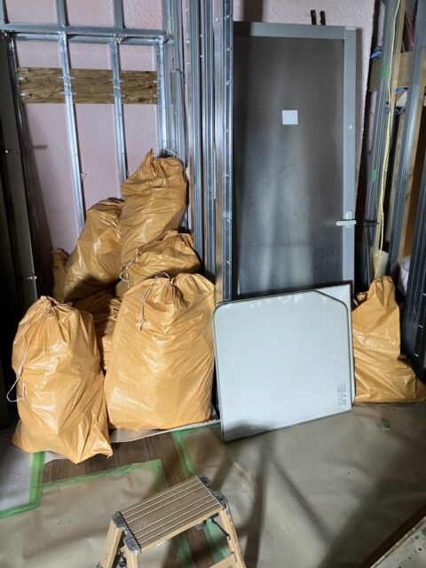 養生した室内に置かれた袋詰めの廃棄物と取り外した扉などの部材
