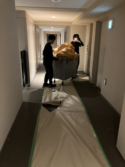 床を養生したマンションの共用廊下で袋詰めの廃棄物を台車に載せて搬出する様子